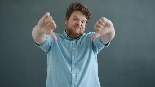 Portrait of Disappointed Guy Showing Thumbsdown Hand Gesture and Shaking Head on Gray Background