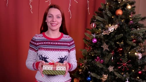 Festive Woman Offering a Christmas Gift Near Tree