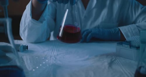 Chercheuse mélangeant une fiole conique avec un liquide rouge, au Ralenti