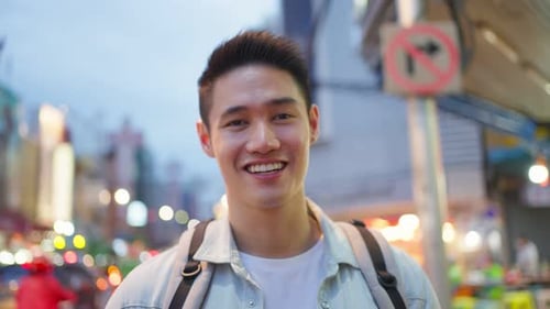 Mochileiro asiático atraente andando pela cidade na estrada noturna.