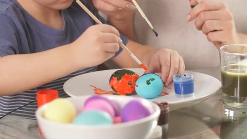 Young Mother and Her Son Having Fun While Painting Eggs for Easter