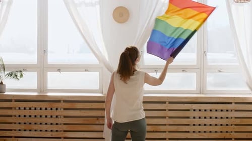 Woman Waving Rainbow Flag in Bright Room