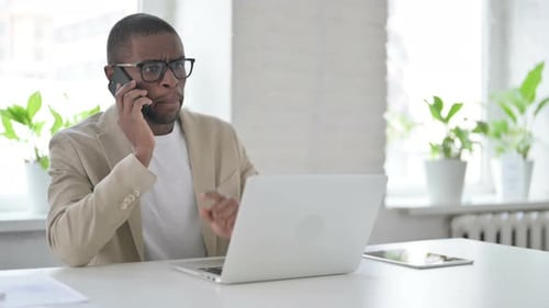 Angry African Man Talking on Smartphone in Office
