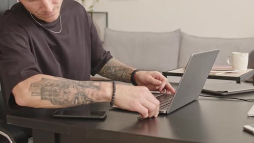 Tattooed Programmer Working on Laptop at Home Office