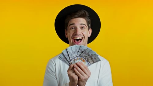 Erstaunter glücklicher aufgeregter Mann zeigt Geld - US-Dollar-Banknoten auf gelber Wand, Symbol