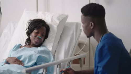 An African Male Doctor Interviews a Patient Lying in a Hospital Bed with an Oxygen Mask