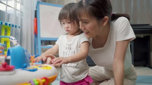 Asiatische glückliche Familie, schöne Mutter und kleines Mädchen spielen zusammen Spielzeug im heimischen Wohnzimmer
