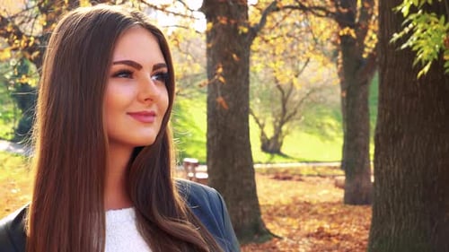 Young Beautiful Woman Looks Around in the Park in Autumn Day