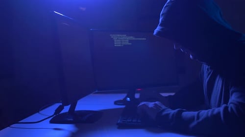 Hooded Figure Typing at Computer in Dark Room