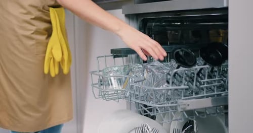 Close-up of Female Hands Opening Dishwasher with Crystal Clear Glasses.