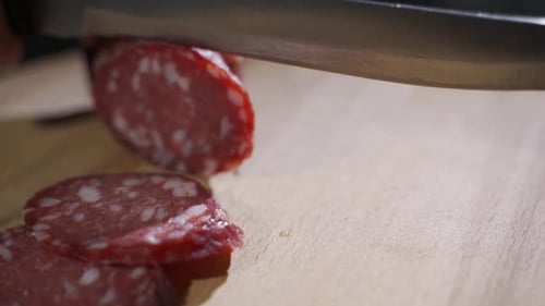 Sharp Knife Cuts Salami on Cutting Board