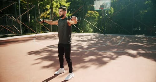 Sporty Man Lifting Weights with Both Hands in a Public Park Biceps Training