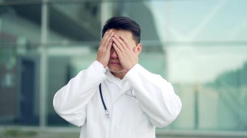 portrait stressful Asian doctor sitting or standing outside a hospital