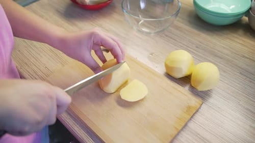 Frau schneidet junge frische Kartoffeln in der Küche mit scharfem Messer auf Holzbrett