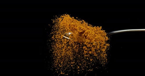 Spoon and Curry Powder falling against Black Background, Slow motion 4K
