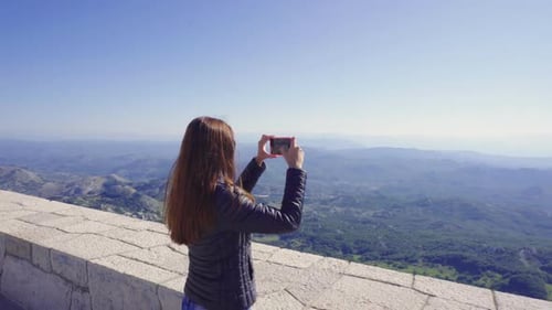 Attractive Girl Photographs a Beautiful Mountain View on a Cell Phone.