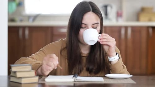 Junges schönes Mädchen macht Einträge in ihr Tagebuch, während sie an einem Tisch sitzt