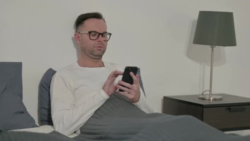 Man Uses Smartphone While Lying in Bed