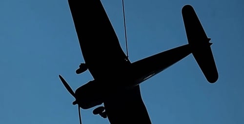 Silhouetted Toy Airplane Spins on String Against Sky