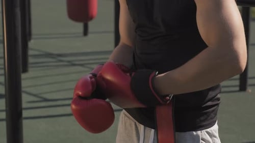Man Puts on Boxing Gloves at Outdoor Gym