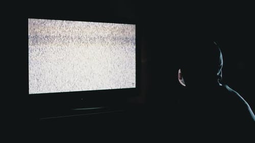 Silhouette d'un homme à capuche et masque médical regardant la télévision avec interférence statique