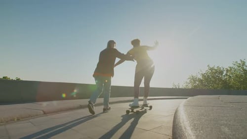 Rear View of Happy Females Learning to Ride Skateboard Outdoors at Dawn
