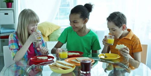 Three Children Enjoying Bread and Juice at Breakfast
