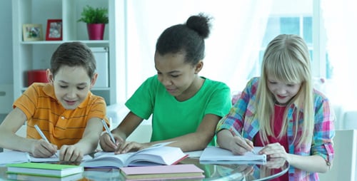 Three Smiling Children Studying Together at Table