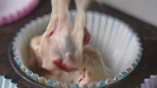 Scooping muffin batter with tasty fruit into colorful wrappers in metal baking tray close up
