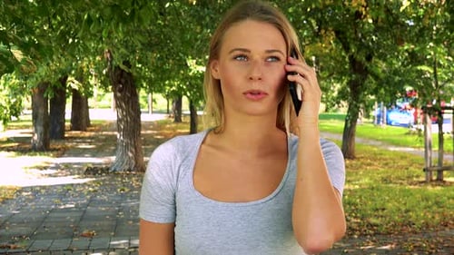 Young Pretty Blond Woman Phones with Smartphone - Park with Trees in Background