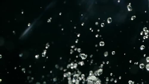 Wassertropfen steigen in der Luft vor schwarzem Hintergrund auf. Zeitlupe Water Splash auf Schwarz
