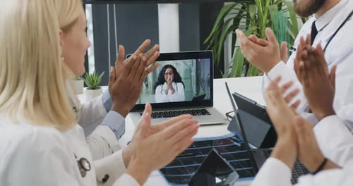 Diversos médicos con experiencia viendo conferencias en línea y saludándose entre sí con aplausos