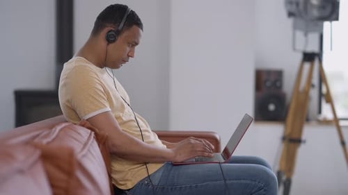 Side View Portrait of Concentrated Young African American Man in Earphones Typing on Laptop Keyboard