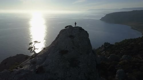 Flight Over of Young Woman Standing on the Top of a Mountain Facing the Sea