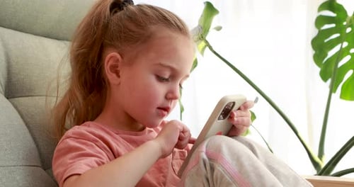 Cute Little Girl with Smartphone Sitting on Armchair Close Up