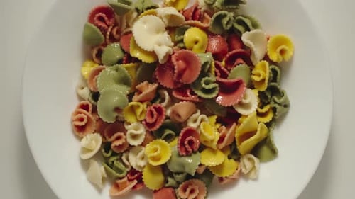 SLOW MOTION: Colourful Rigate Pasta Falling Into A White Plate - Top View