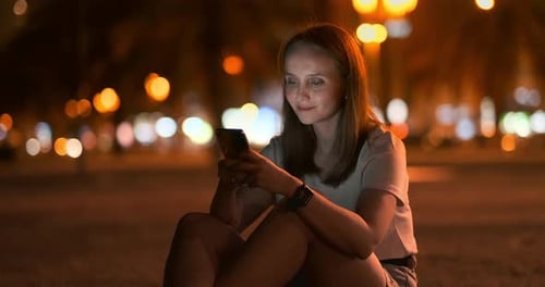 Young Girl in the Night City Writes Text Messages in a Smartphone
