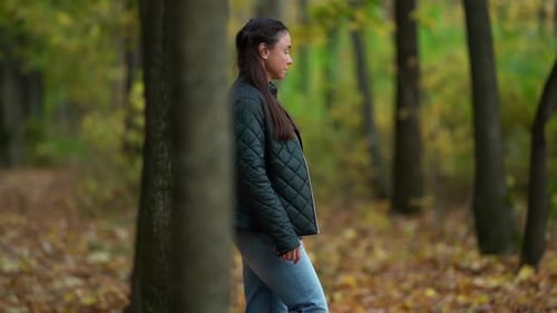 A Middle-aged Woman with Dark Hair Enjoys Nature in an Autumn Forest. Smiling and Walking Among the