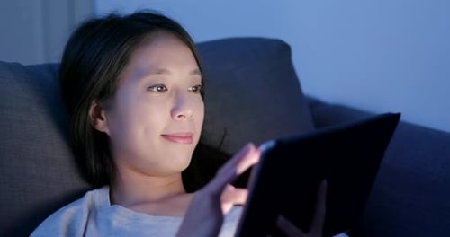 Woman use of tablet computer and lying on sofa at night