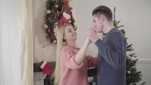 Happy Young Caucasian Couple Dancing in Front of New Year Tree at Home. Smiling Man and Woman in