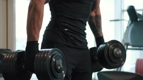 Muscular Man Lifting Heavy Dumbbells in Gym