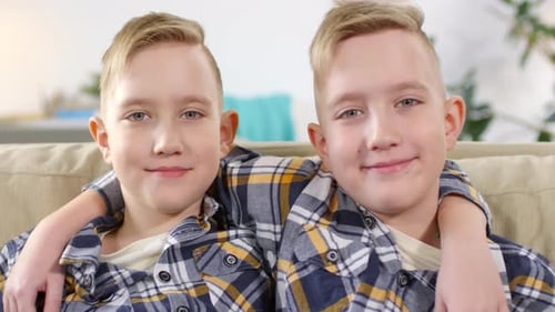 Two Young Brothers Smiling Together on Couch Indoors