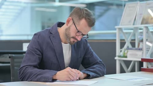 Man Writes and Thinks at Desk in Office
