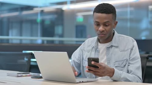 Young Adult Working on Phone and Laptop in Office