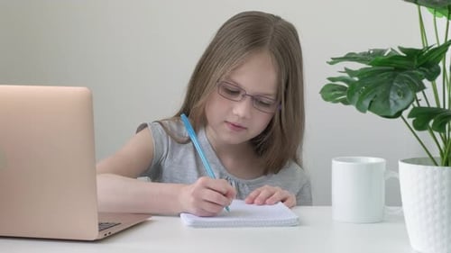 Little School Girl Wearing Glasses Sitting at Table Doing Homework