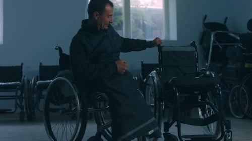 Side View of One American Male Workers in a Workshop at a Factory Making Wheelchairs Sitting at a