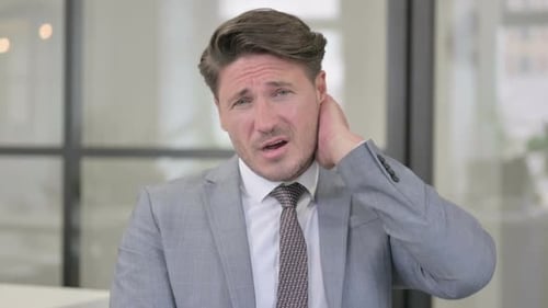 Mature Man Massaging Stiff Neck at Workplace