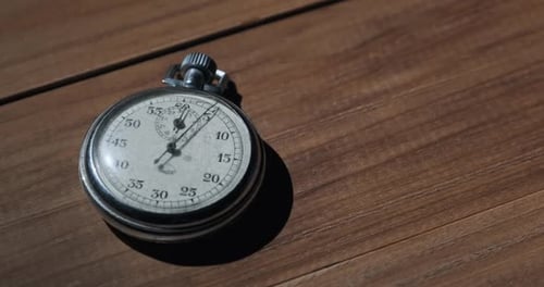An Antique Stopwatch Lies on Wooden Table and Counts the Seconds