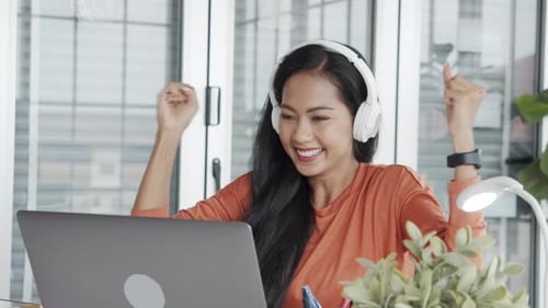 Woman Celebrates Success at Laptop with Headphones