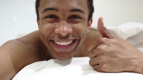 Pouces levés par un homme africain heureux allongé dans son lit sur le ventre